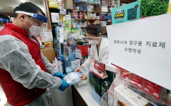 Korea from Jan. 13 will start prescribing oral medication for COVID-19. Pictured is an official (left) from the public health center of Incheon's Bupyeong-gu Office on the morning of Jan. 12 delivering the pills to a pharmacist in the same district as part of a simulation.